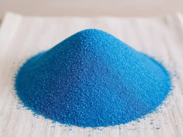 Detalle de arena fina azul sobre una superficie clara, destacando su textura y color vibrante.