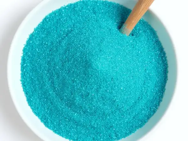 Muestra de arena fina azul caribe en un cuenco con elementos marinos, destacando su grano y color
